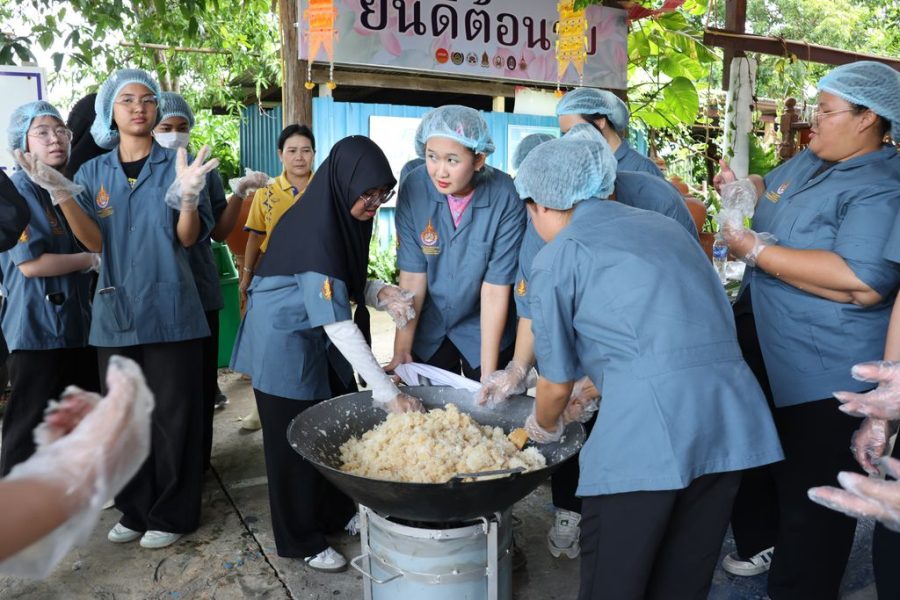 นักศึกษาช่วยกันนำวัตถุดิบใส่กระทะเพื่อเตรียมกวนข้าวเหนียวแดง